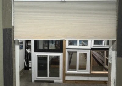 Close-up of a window frame with a beige blinds, showcasing multiple framed windows in the background and a wooden ledge below.