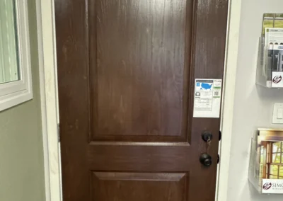 A wooden door with a curved top and two lower panels, marked as Signet Knotty Alder Series, with a window and brochures nearby.