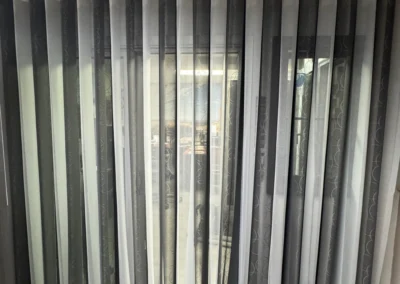 A set of vertical, two-tone curtains partially covering a window, revealing a hint of caution tape on the floor beside a chair.